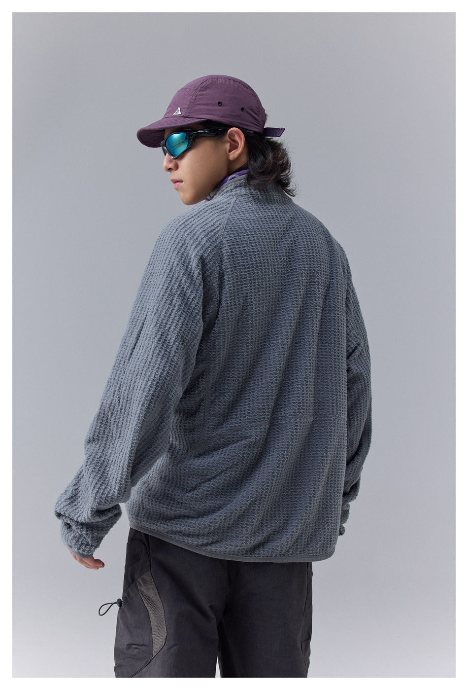 Rear view of a model wearing a gray textured jacket and black cargo pants.