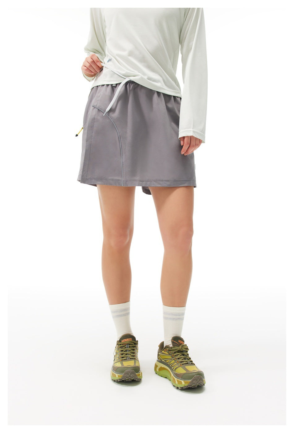 Front view of a model wearing a gray athletic skort with a drawstring waist and curved seam detail.