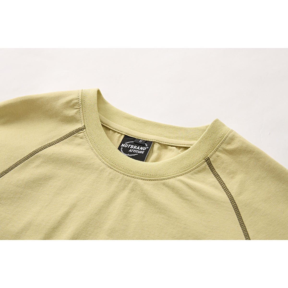 Close-up of a pale yellow T-shirt's ribbed crew neck, raglan seams and inner black label.