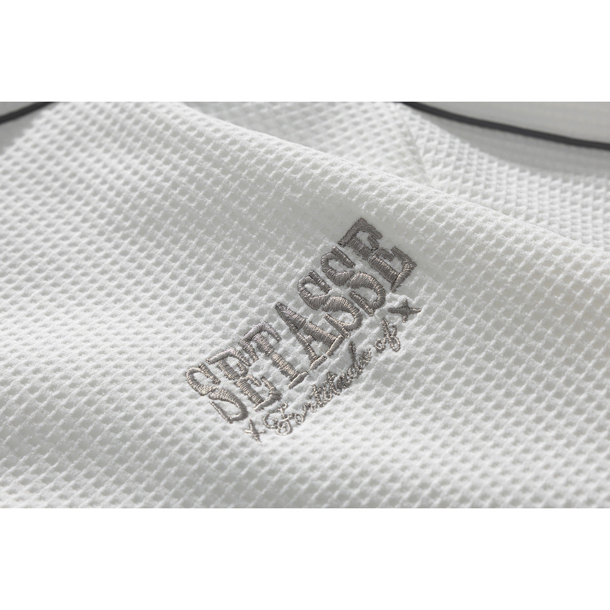 Close-up of gray embroidered lettering on the textured white polo fabric.