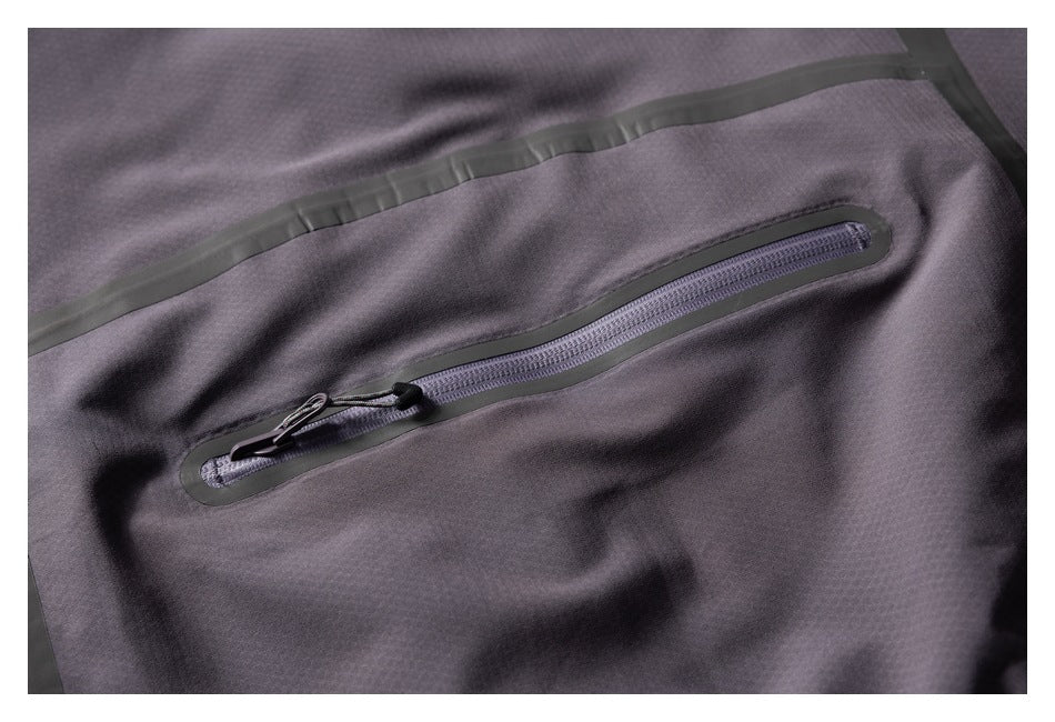 Close-up of a dark charcoal jacket with a diagonal zippered pocket and dark seam taping.