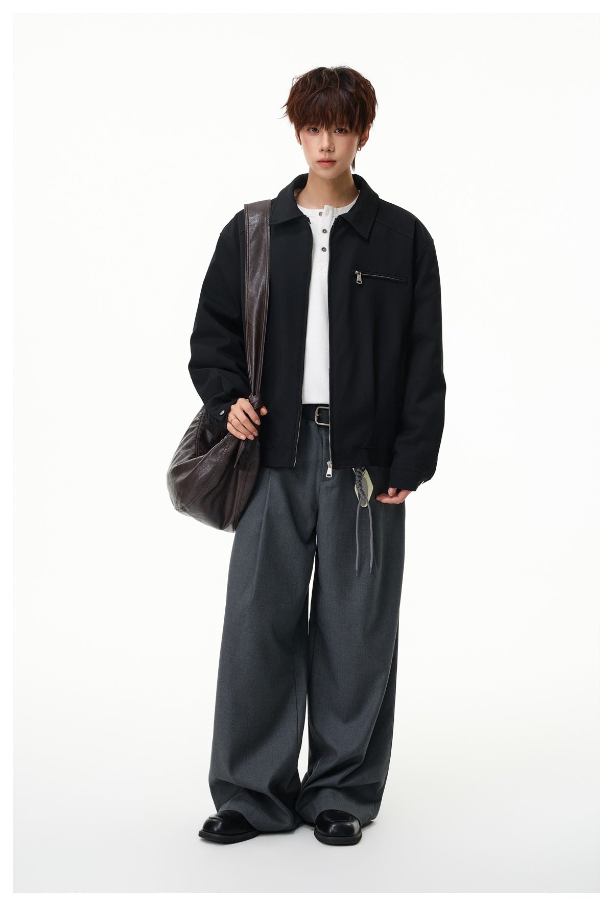 Full-length view of a model wearing a black zip jacket over a white shirt and wide gray trousers.