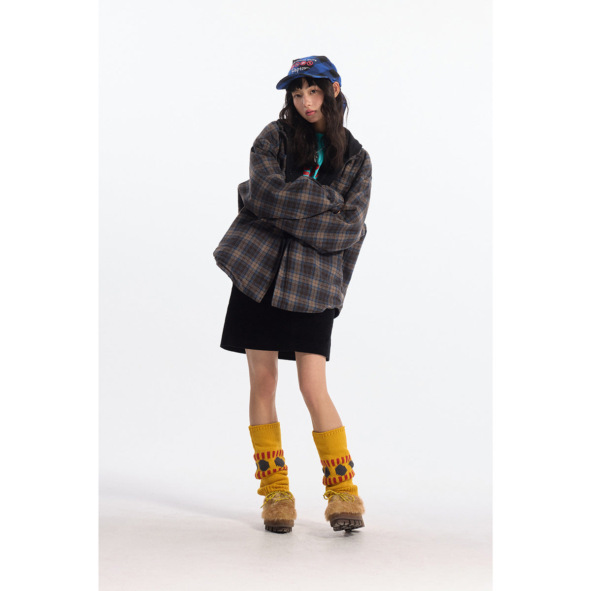 Model wearing an oversized brown-and-blue plaid shirt jacket over a black skirt, with yellow leg warmers.