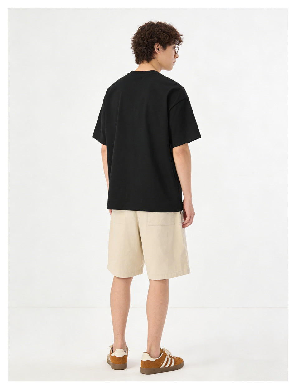 Rear view of a model wearing a black short-sleeve T-shirt and light beige shorts with back pockets.