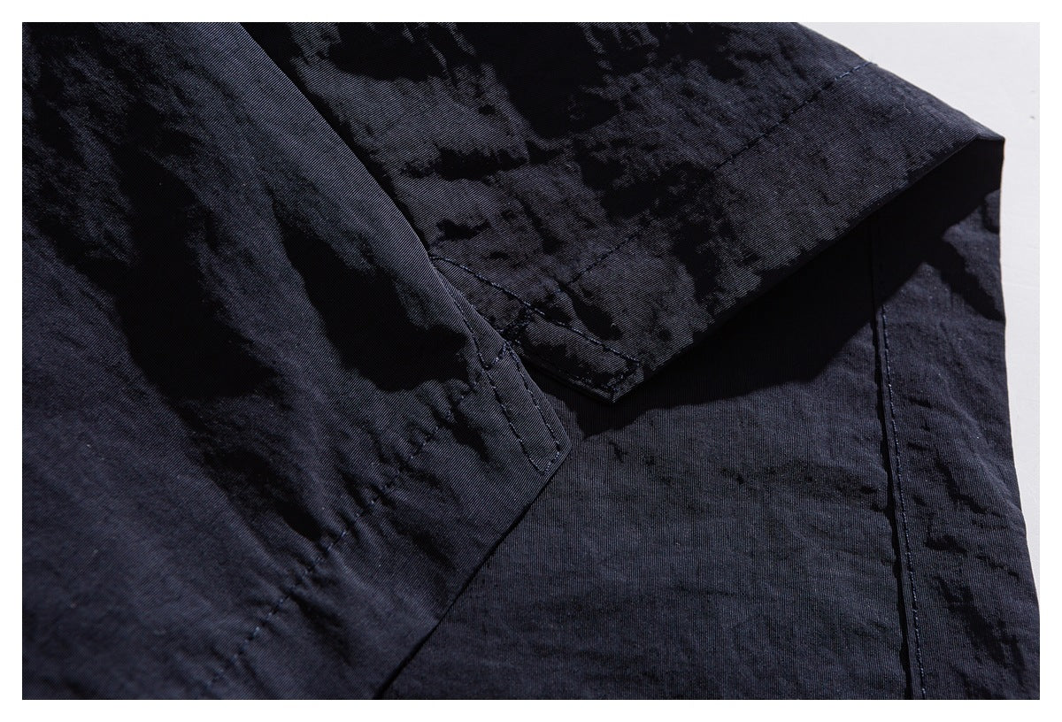 Close-up of dark patterned garment fabric with a folded edge, seam, and visible stitching.