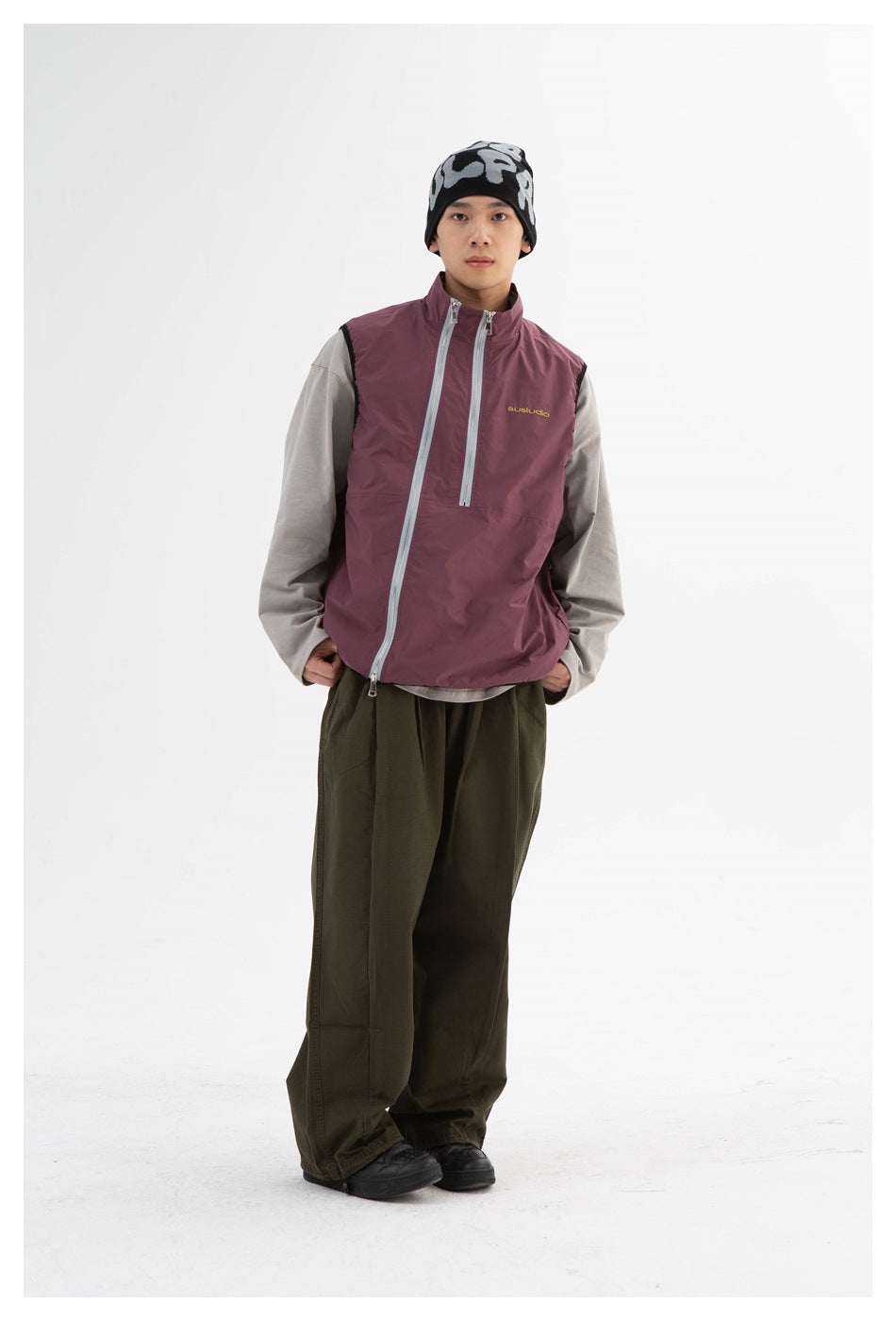 Model wearing a plum stand-collar vest with gray double zippers over a gray long-sleeve top and olive trousers, front view
