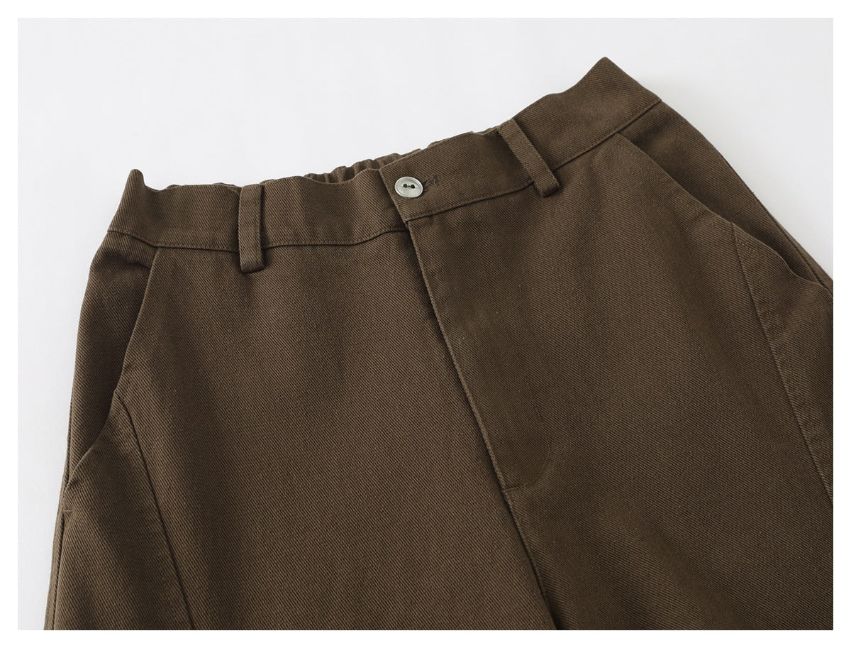 Close-up of brown trousers showing the front waistband, button, belt loops, fly and pocket.