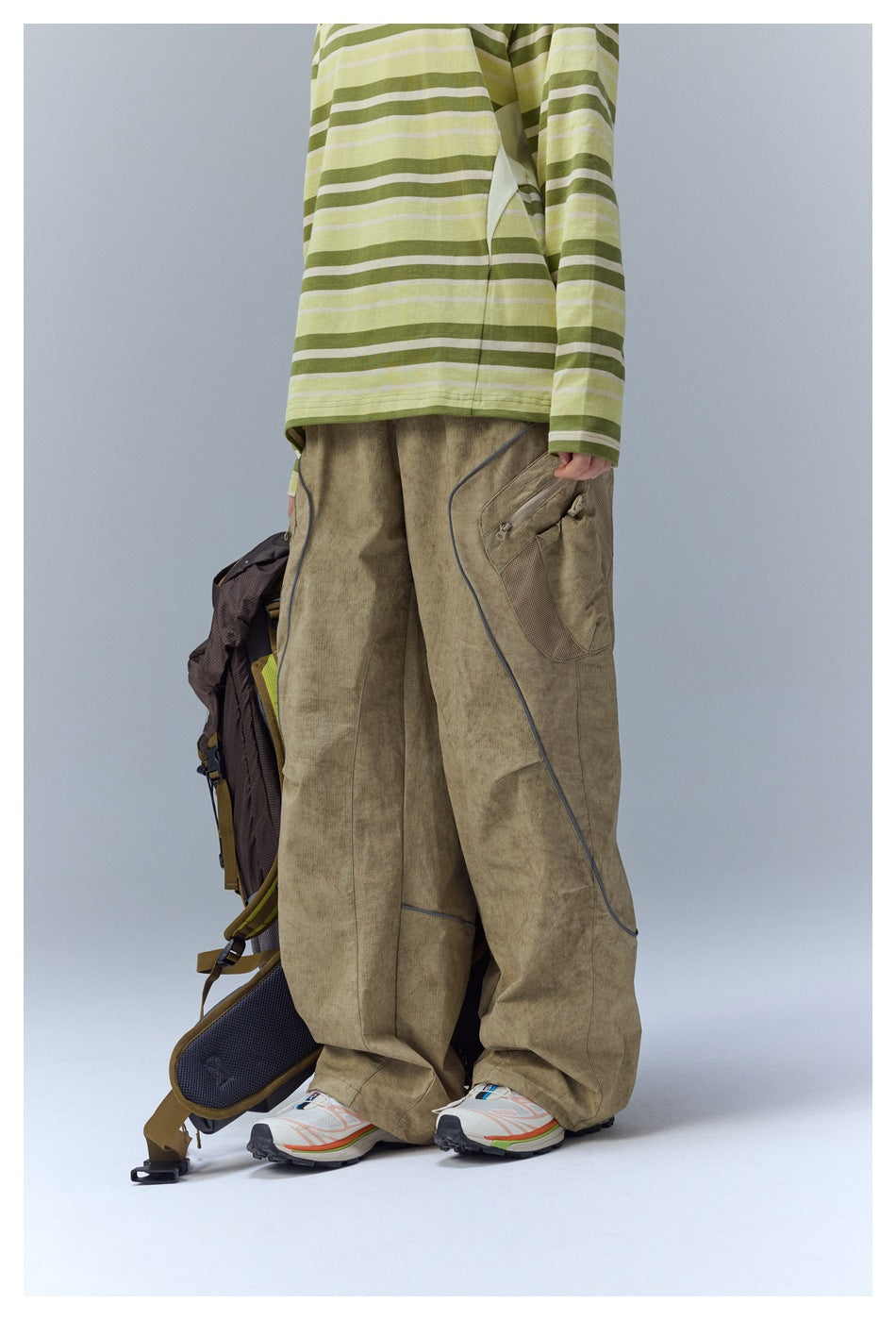 Angled side view showing the khaki cargo pants' zip pockets, mesh pocket panel, and curved piping.