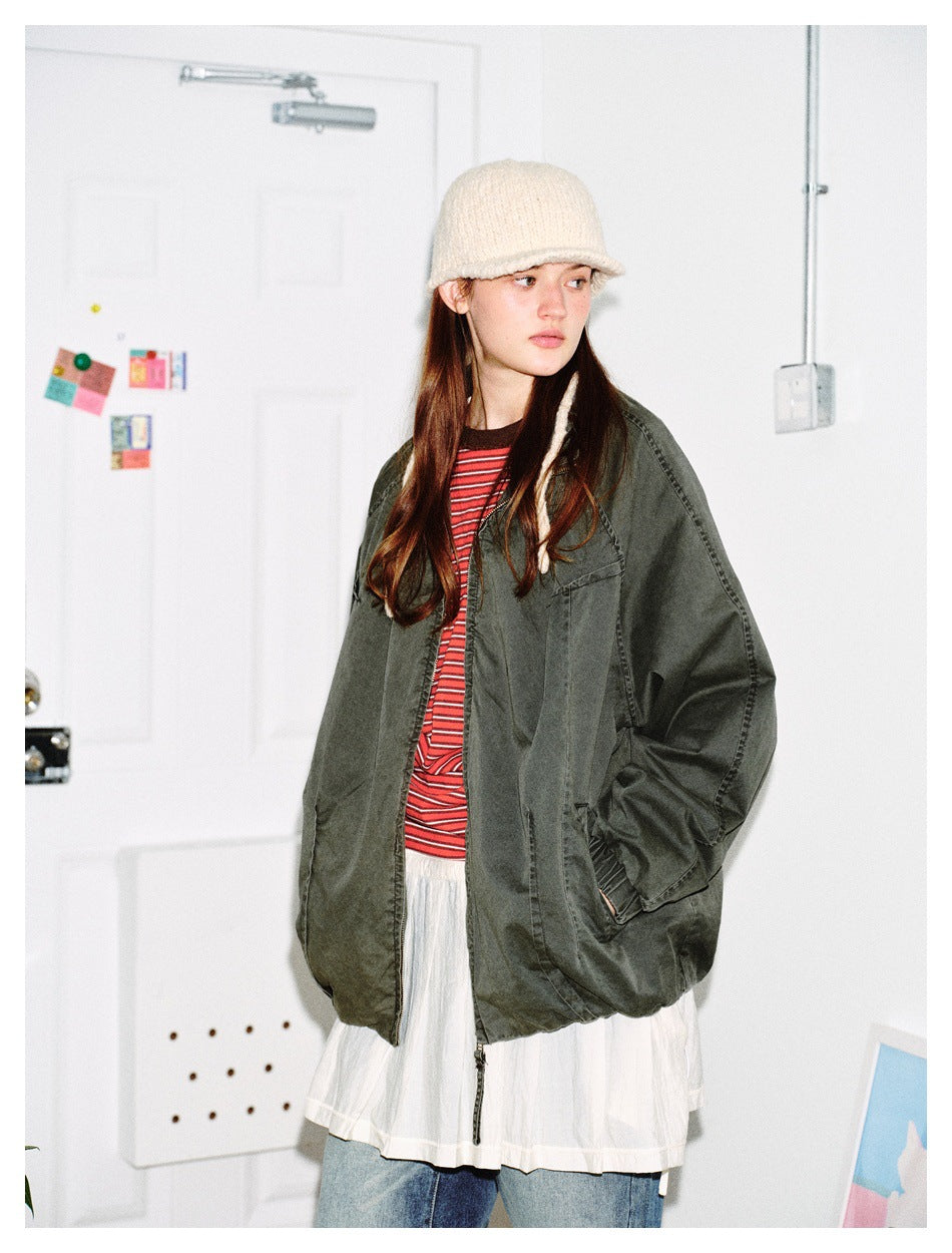 Model wearing an oversized green zip jacket open over a red striped tee, white skirt and jeans, turned to the side