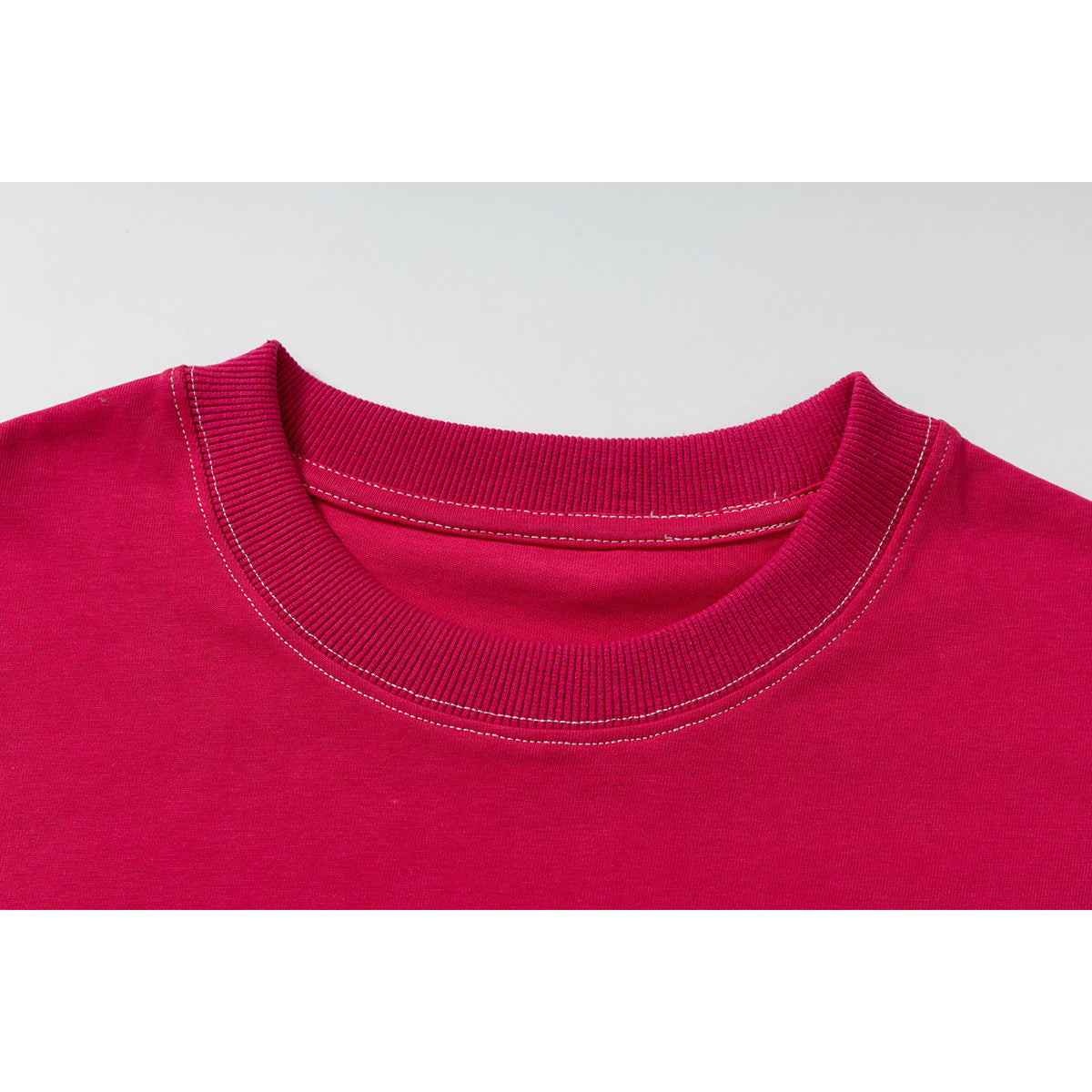 Close-up of a bright magenta T-shirt’s ribbed crew neckline with contrast stitching.