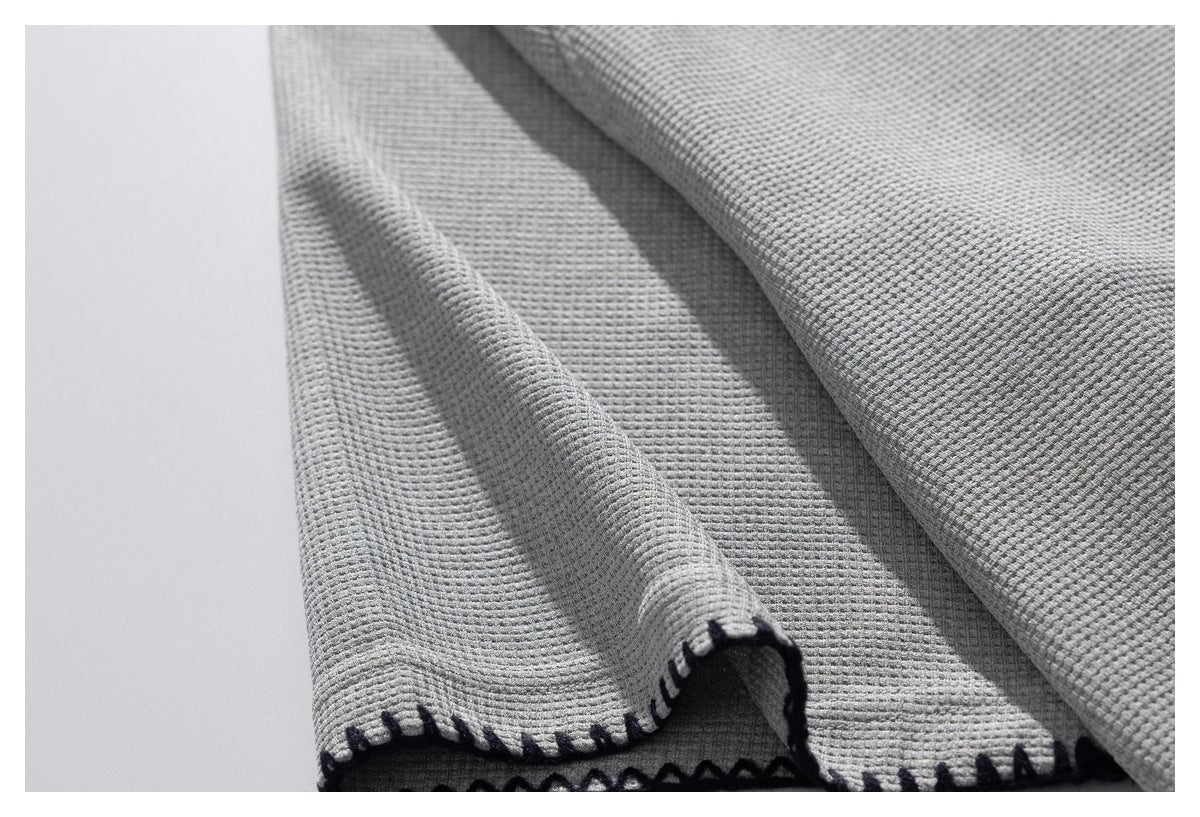 Close-up of the light gray shirt's textured fabric and folded edge with dark contrast stitching.