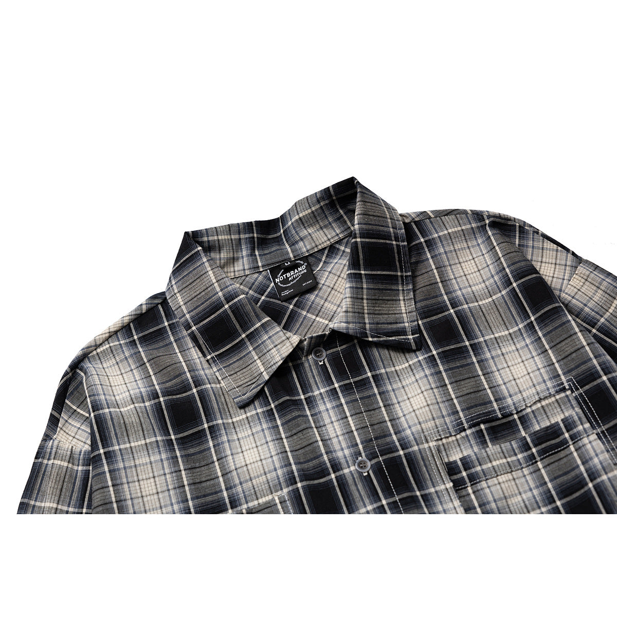 Close-up of a black, gray, and cream plaid shirt showing its pointed collar, buttons, and chest pocket.