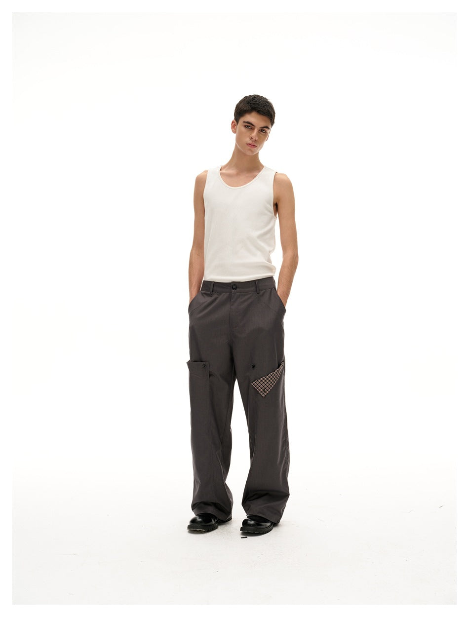 Model wearing a white tank top and charcoal wide-leg trousers with buttoned utility pockets and plaid accents.