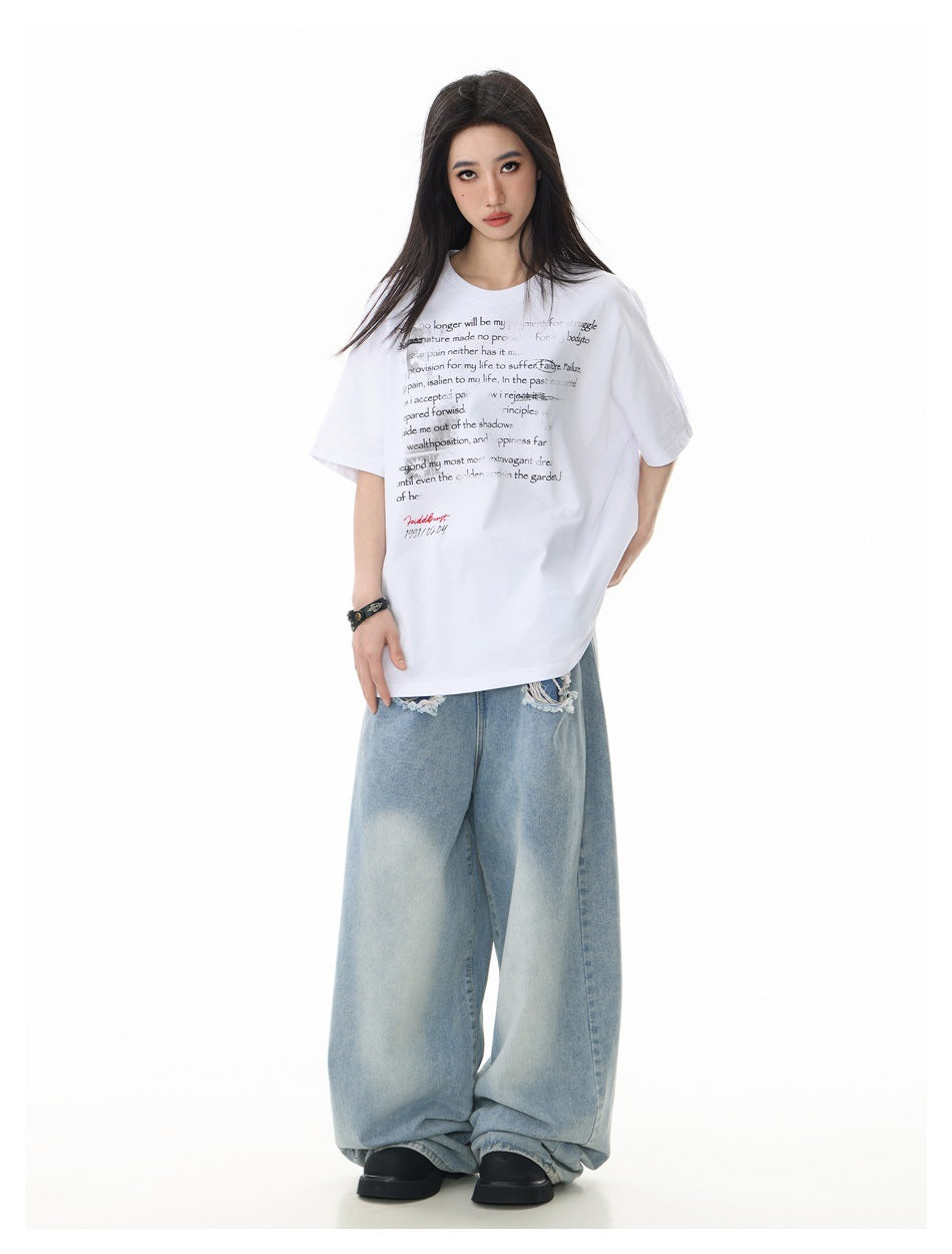 Model wearing an oversized white T-shirt with layered black text and loose light-wash jeans, front view.