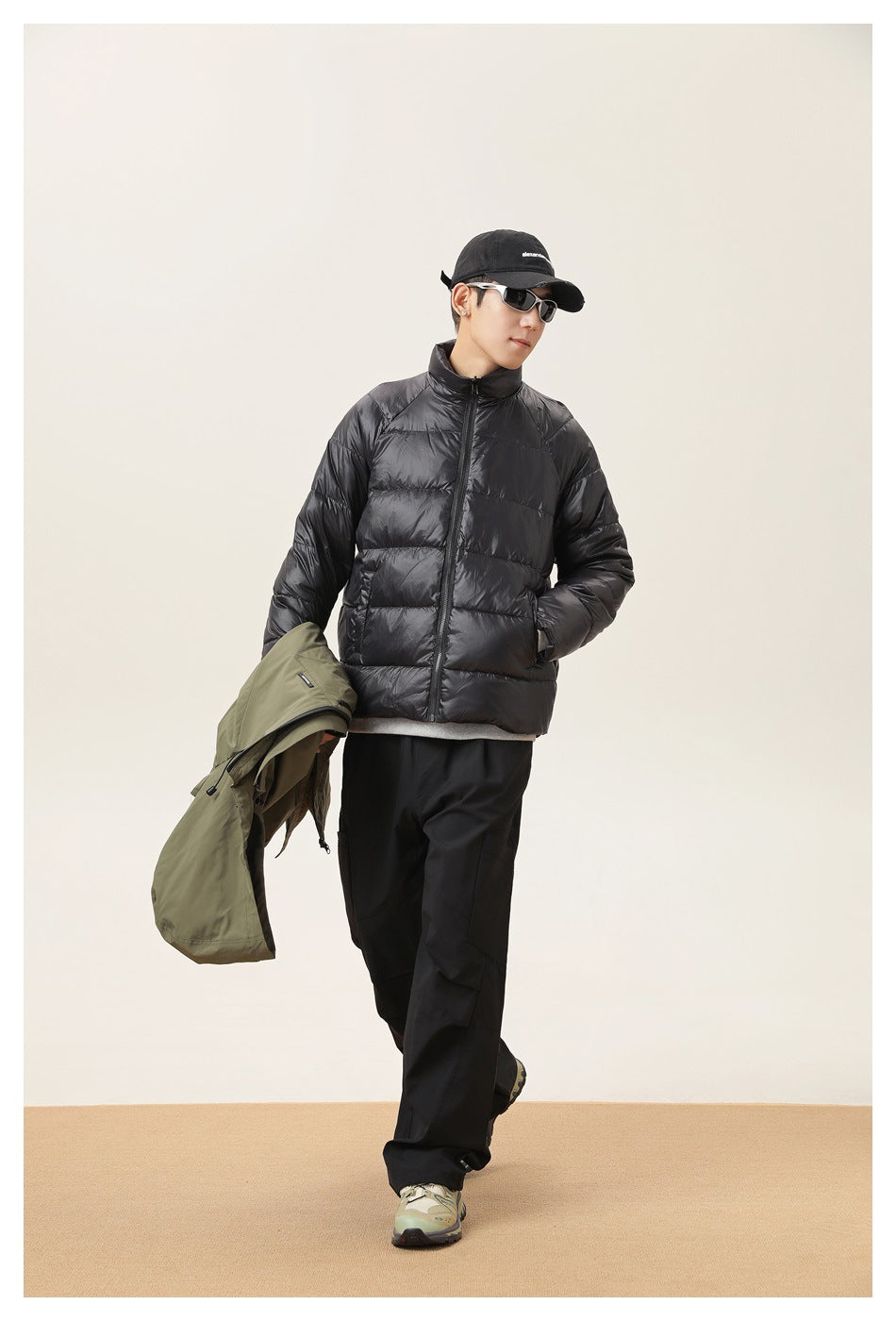 Model wearing a black quilted puffer jacket and carrying an olive hooded jacket.