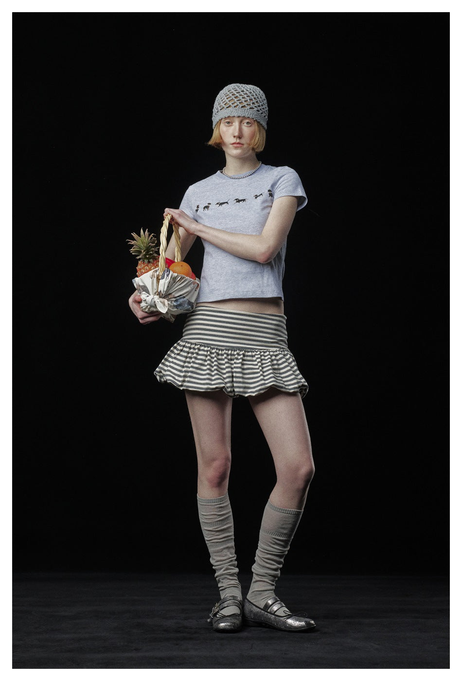 Model wearing a pale gray dog-print T-shirt, gray-and-white striped ruffle skirt and open-knit gray beanie.