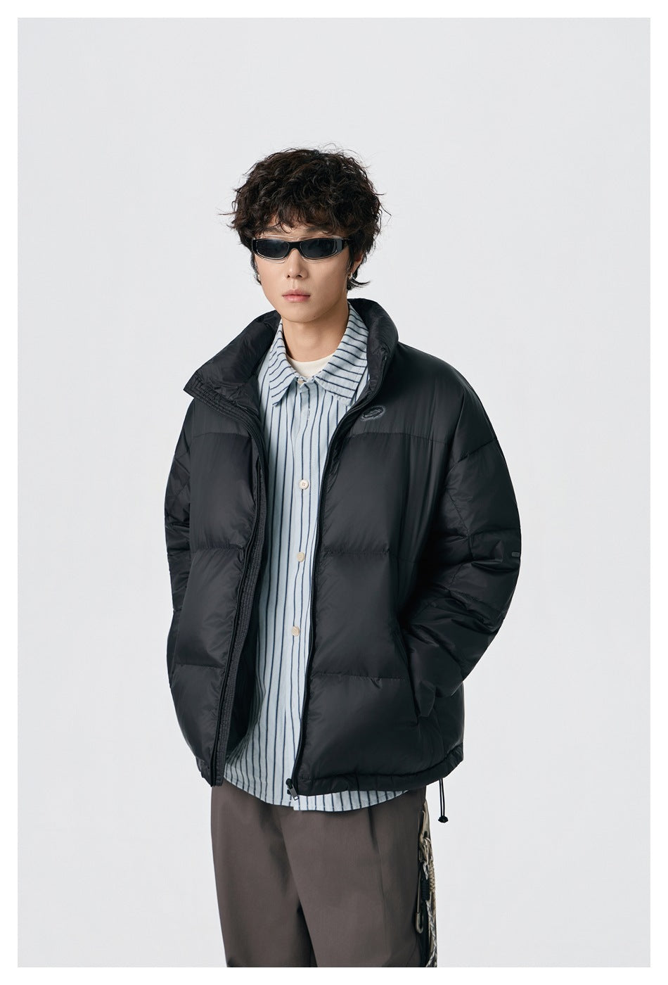 Model wearing black puffer jacket open over a blue striped shirt, close-up of stand collar and chest patch