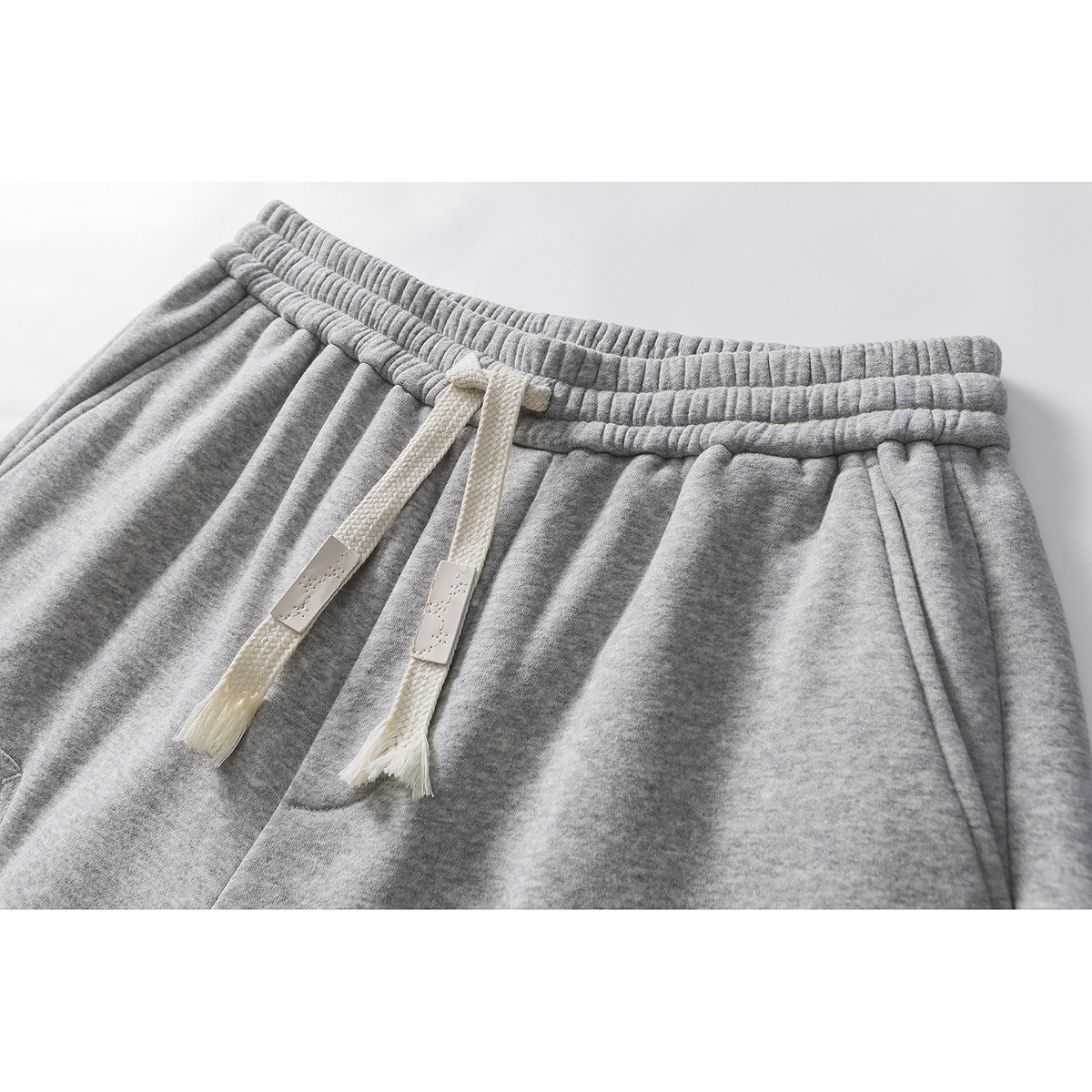 Close-up of gray sweatpants showing the elastic waistband, cream drawstrings, and upper front.