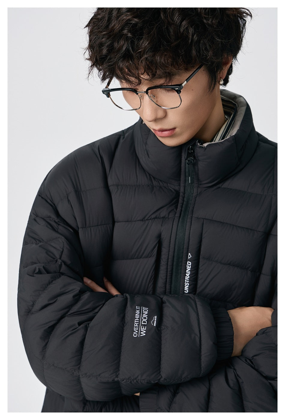 Close-up of a model wearing the black quilted jacket with arms crossed, showing the zipper, chest tape and sleeve print