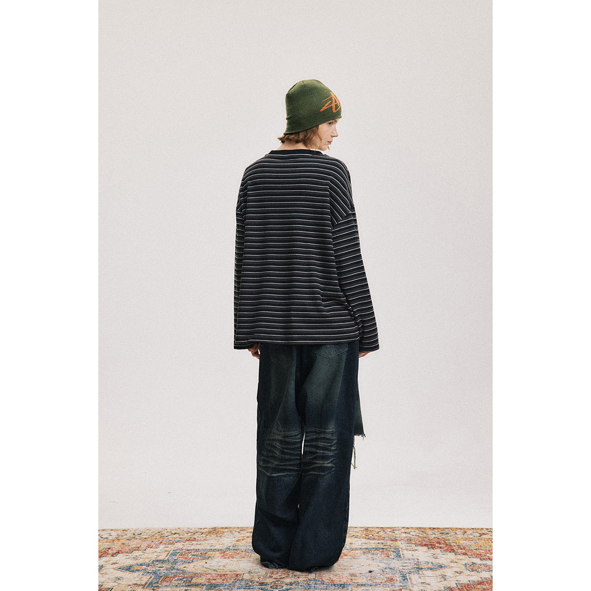 Back view of a model wearing a black shirt with thin white stripes and loose dark jeans.
