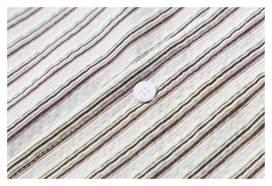 Close-up of narrow dark stripes and a white button on cream shirt fabric.
