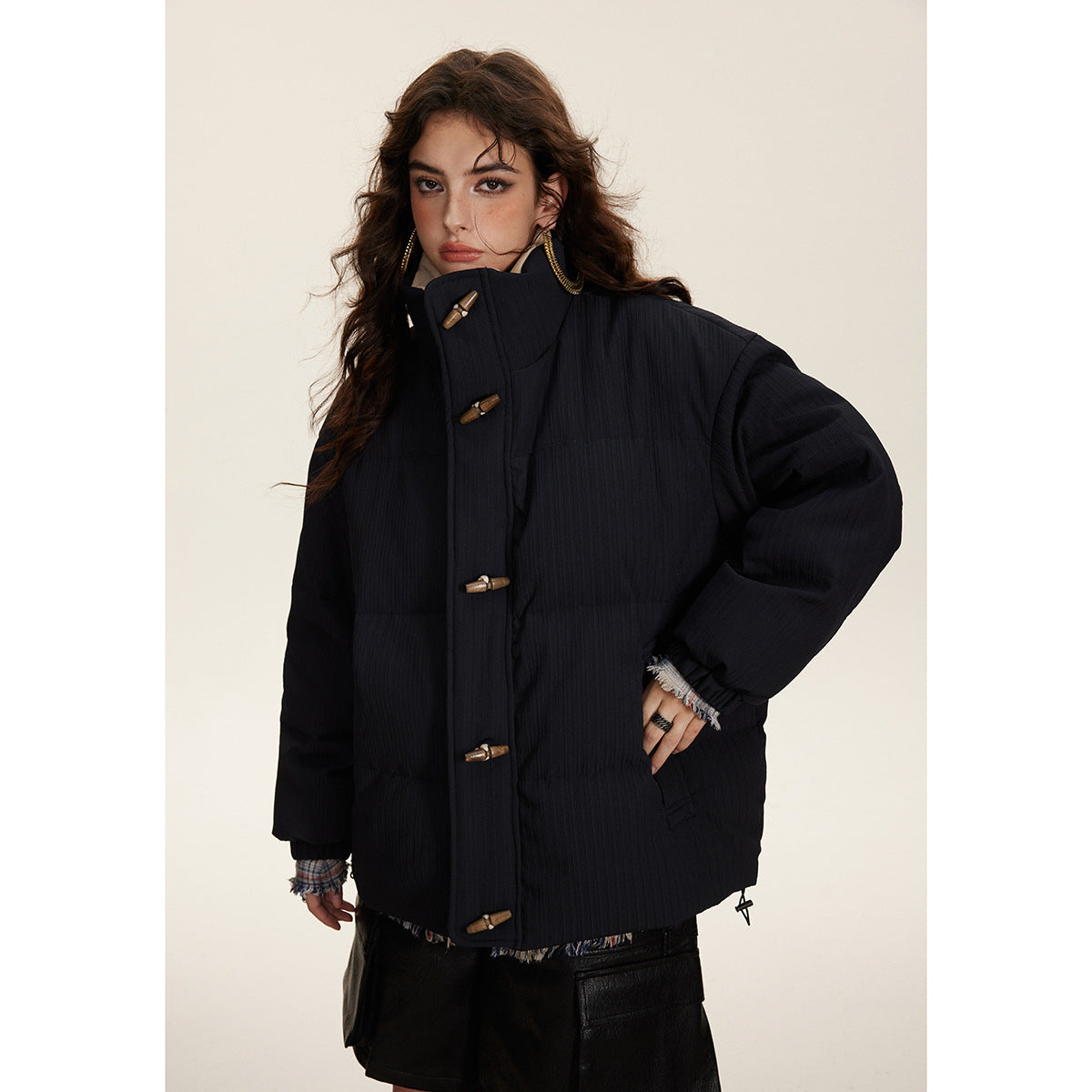 Model wearing a dark padded jacket with a high collar and wooden toggle closures.