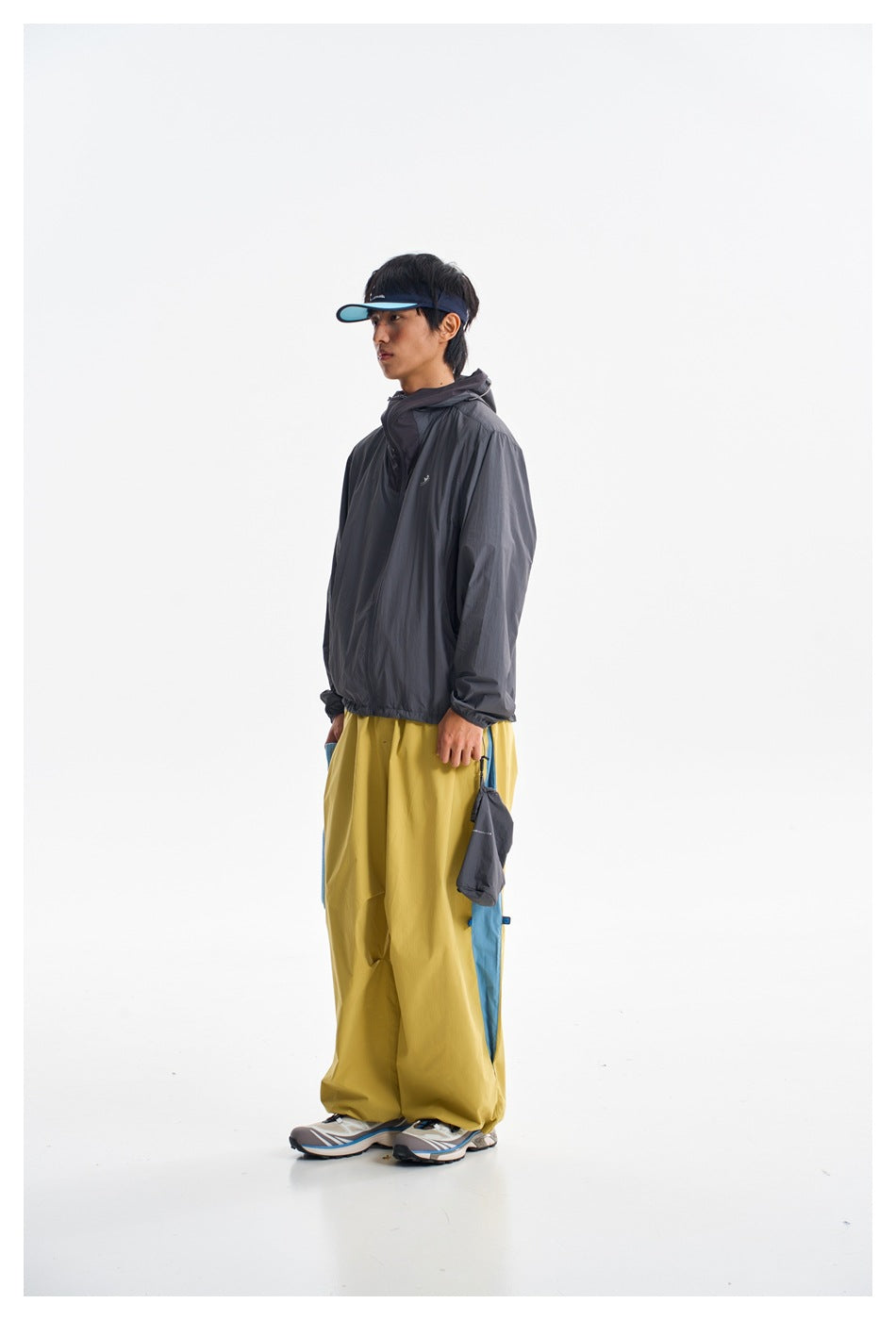 Full-length side view of a person in a charcoal hooded jacket and mustard-yellow pants with blue side panels.