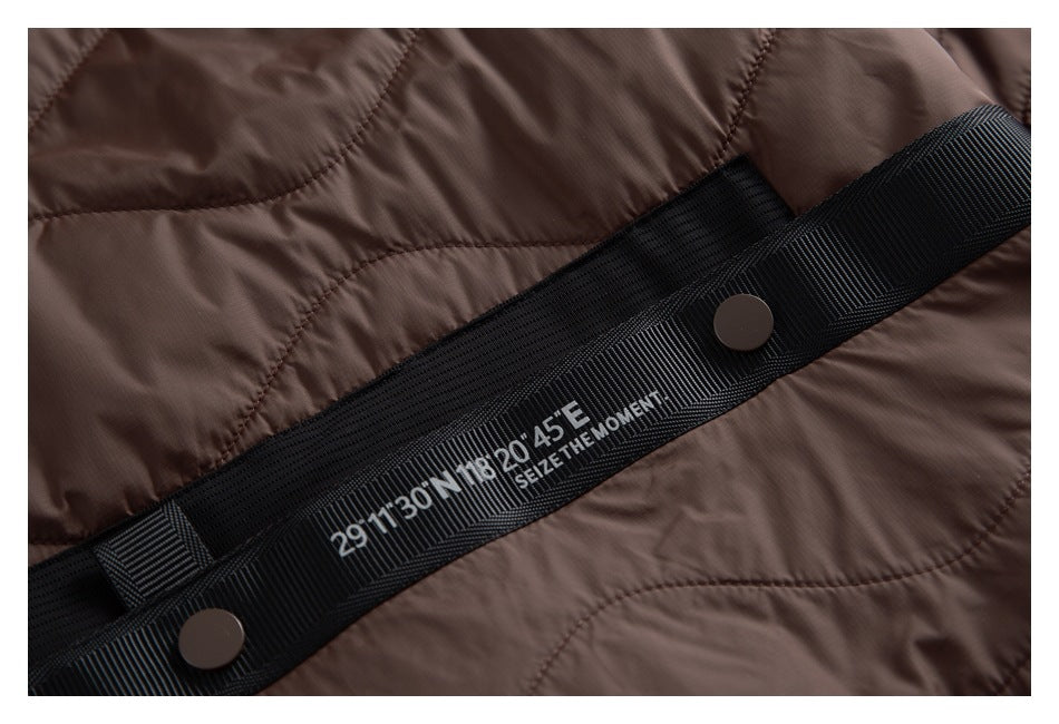 Close-up of a brown quilted garment with a black strap, dark snaps, and white coordinate-style lettering.