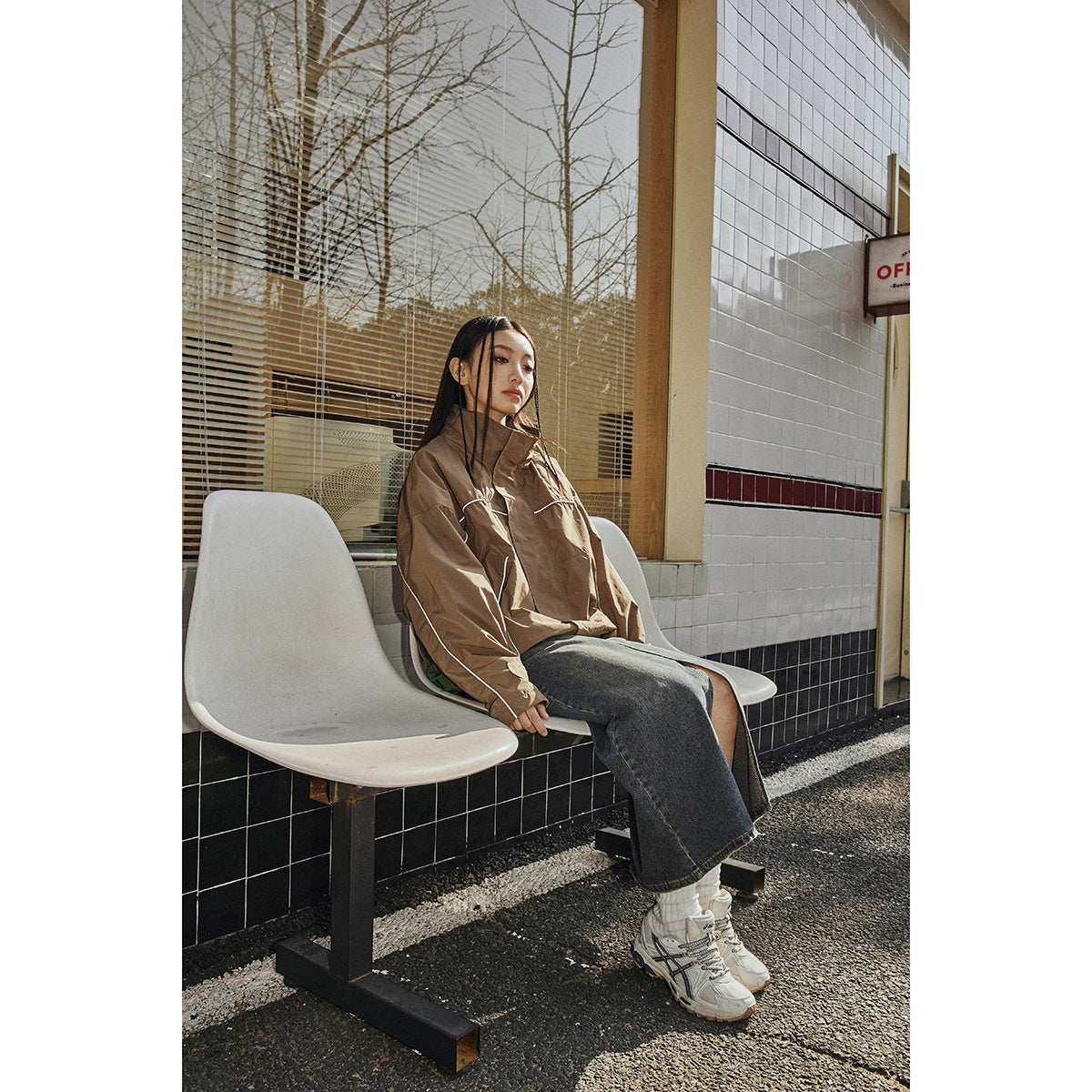 Model seated in a brown oversized jacket with white piping and a raised collar, shown from the front.