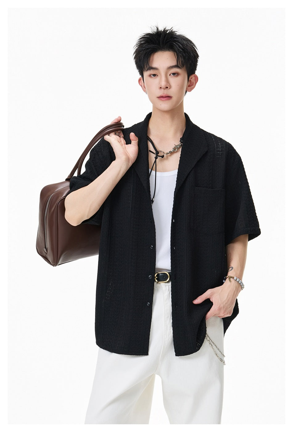 Close-up of model wearing black textured open-knit short-sleeve shirt open over a white tank, holding a brown bag