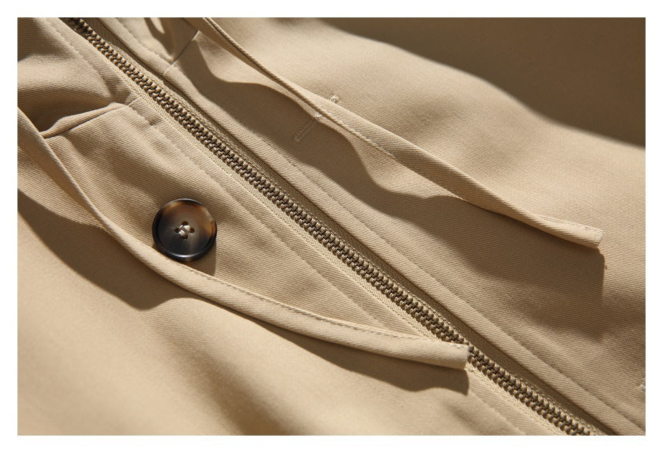 Close-up of a tan jacket showing its diagonal metal zipper, dark button, and stitched panels.