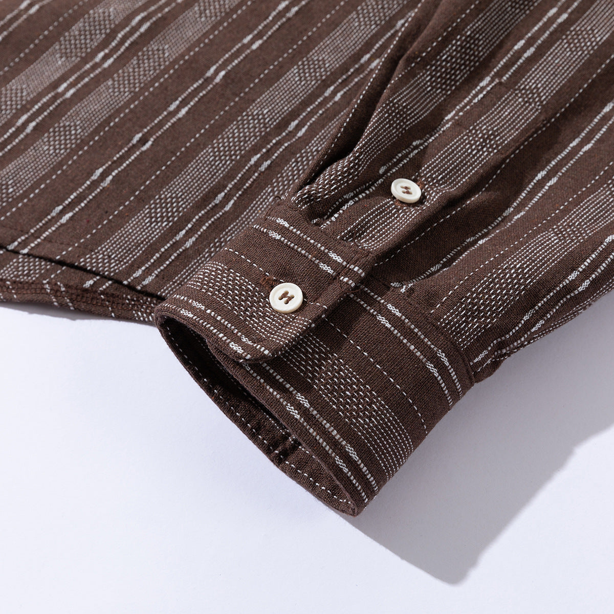 Close-up of a brown shirt cuff with cream buttons and irregular white stripe patterns.
