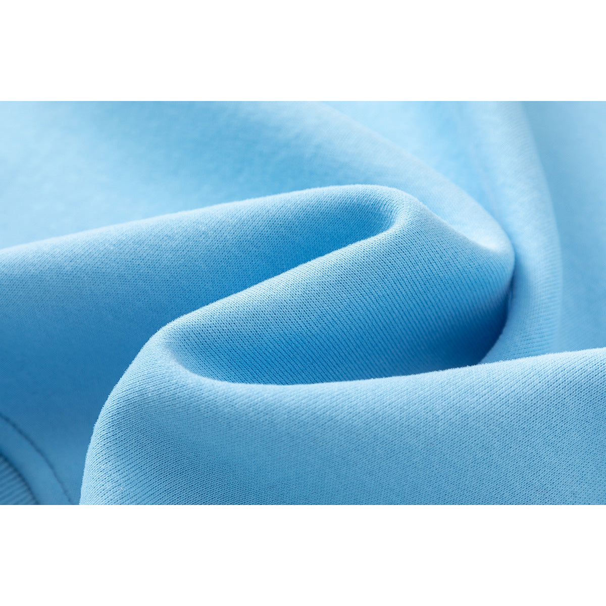 Macro view of light blue sweatshirt fabric gathered into soft folds, showing its knit texture.