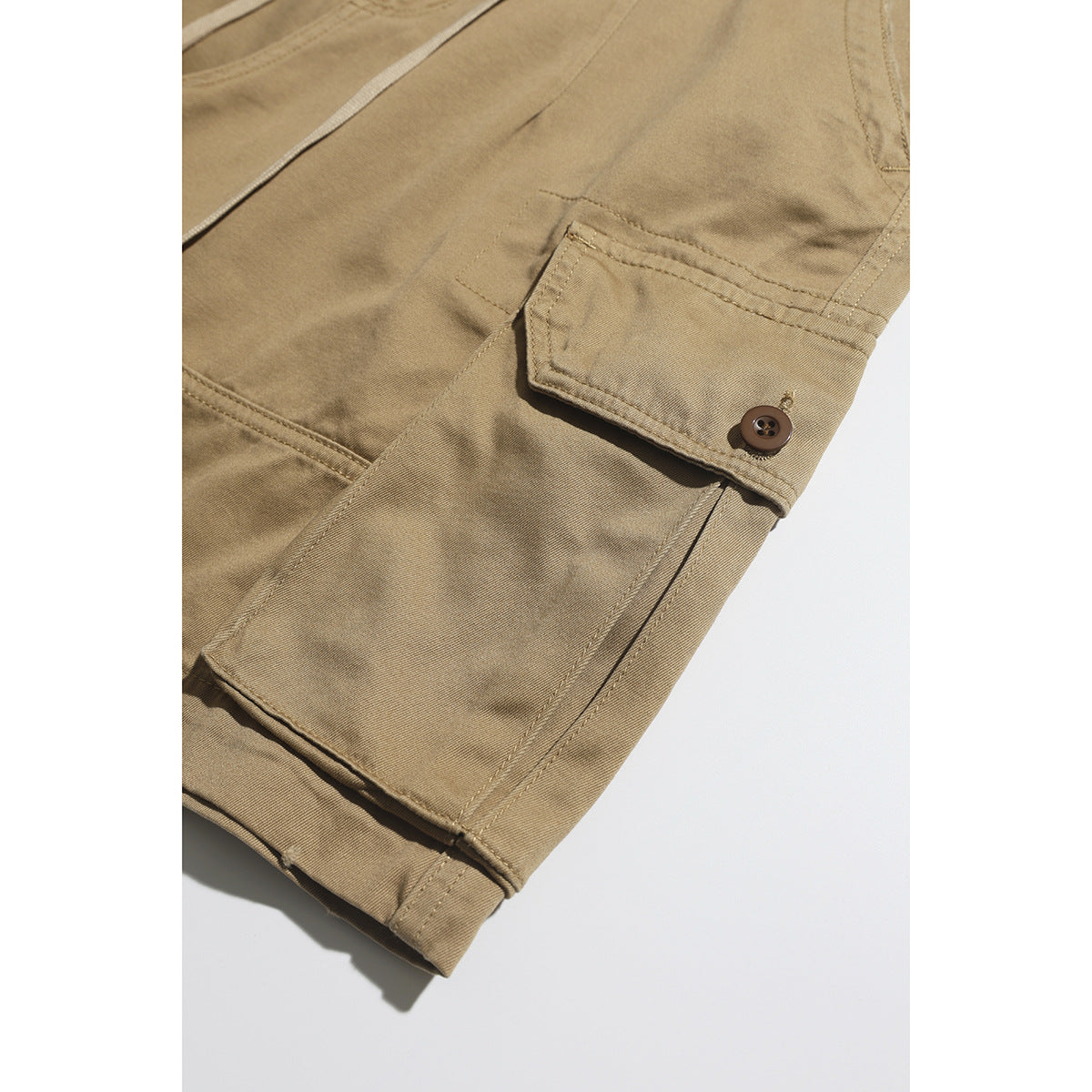Close-up of tan shorts with a buttoned flap cargo pocket and stitched hem.