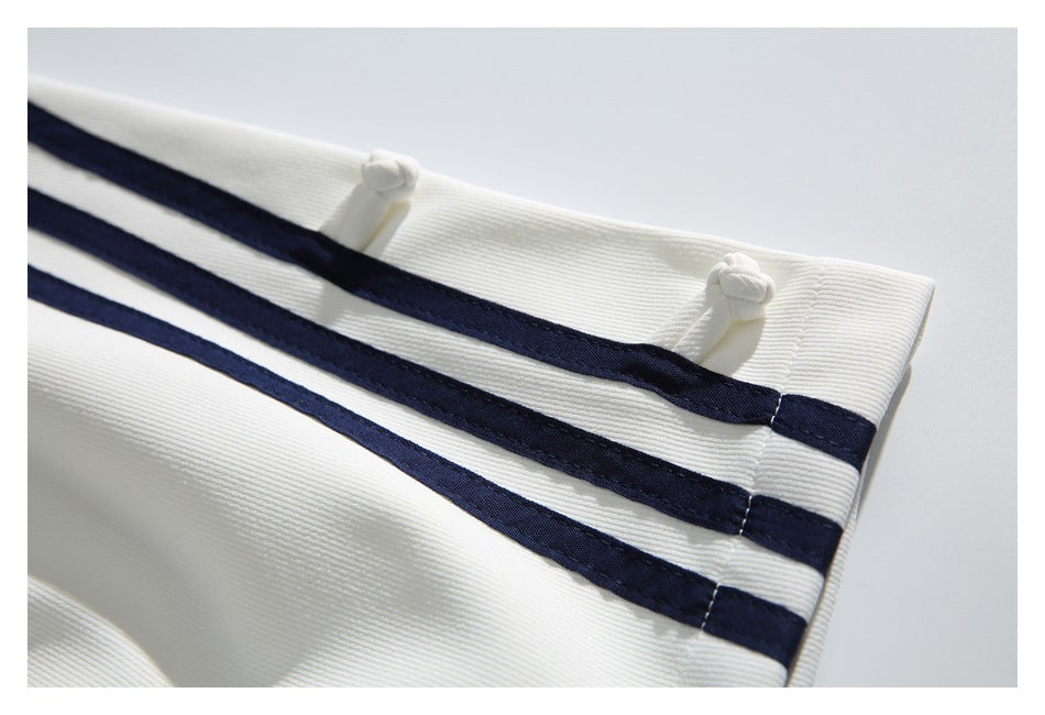 Close-up of a white trouser cuff with navy stripes and knotted white fasteners.
