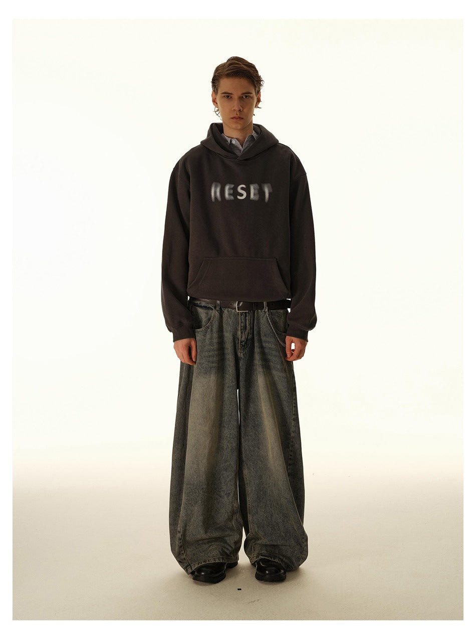 Front view of a model wearing a dark charcoal hoodie with blurred light chest lettering and oversized gray jeans.