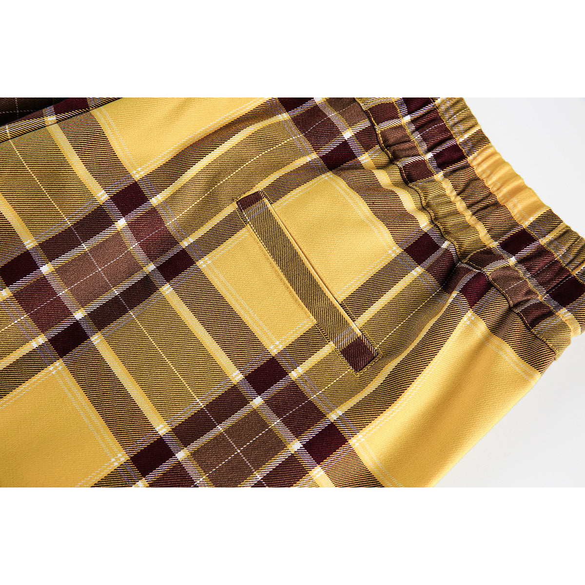 Close-up of mustard, brown and burgundy plaid pants showing a slanted pocket and elastic waistband.