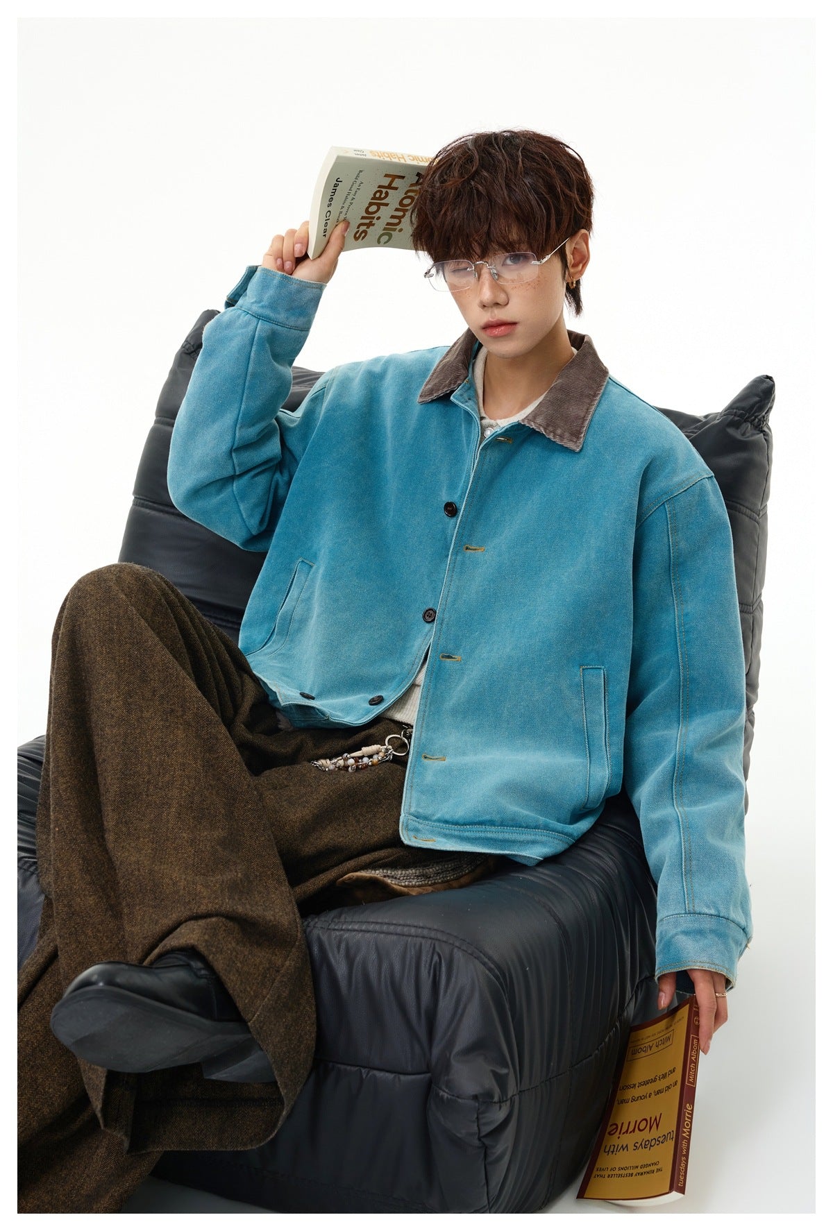 Model seated in a teal button-front jacket with a brown corduroy collar and oversized brown trousers.