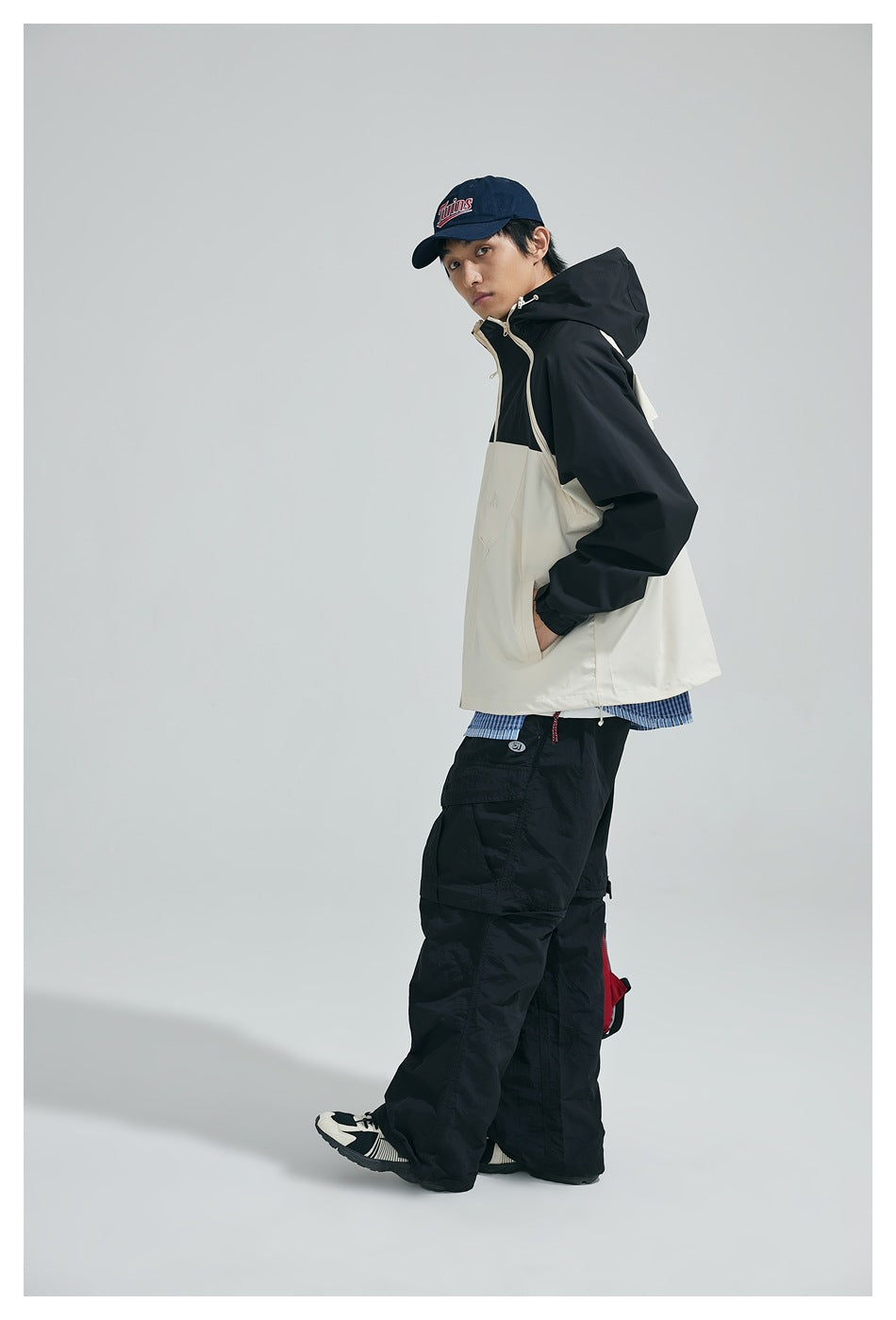 Model wearing a cream-and-black hooded jacket, shown from the side with its front and hood visible.