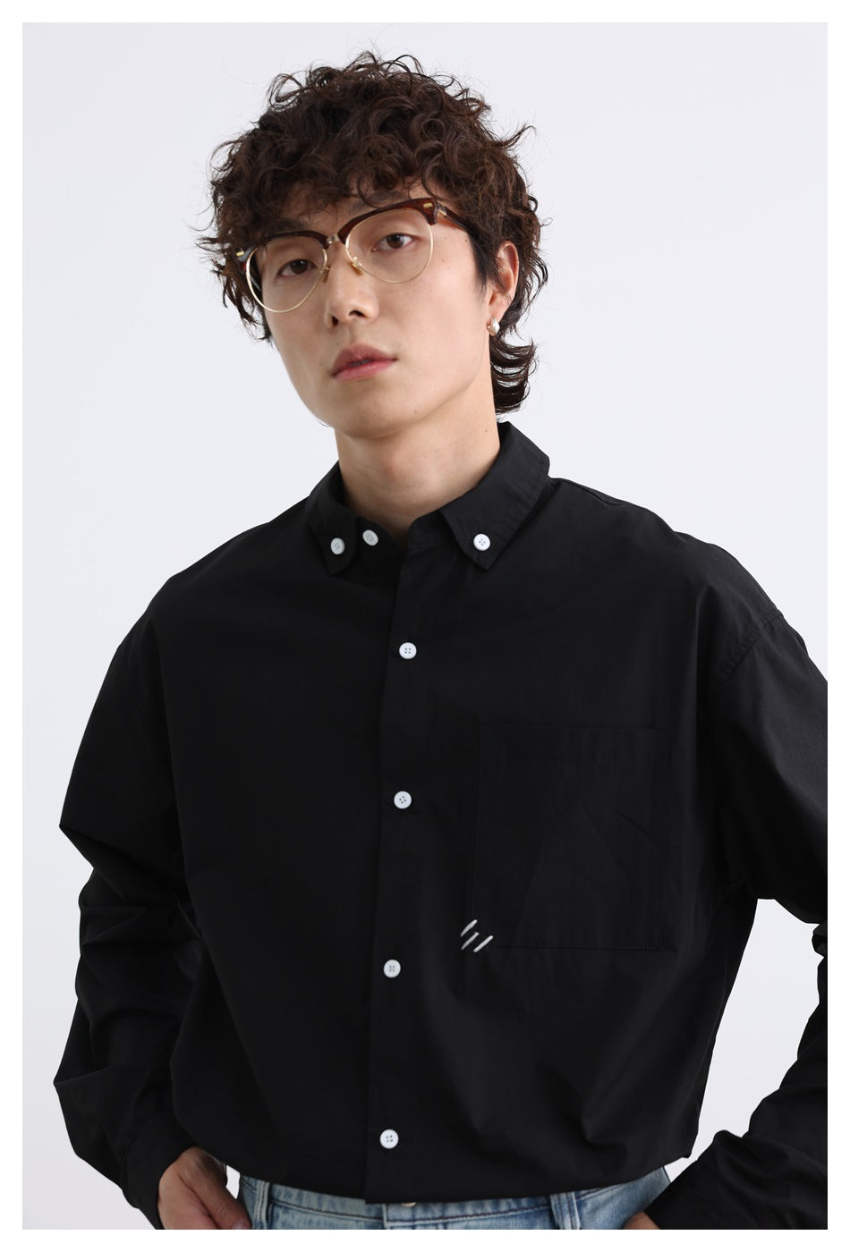 Close view of a model wearing a black button-down shirt with white buttons, a chest pocket, and a small stitched mark.