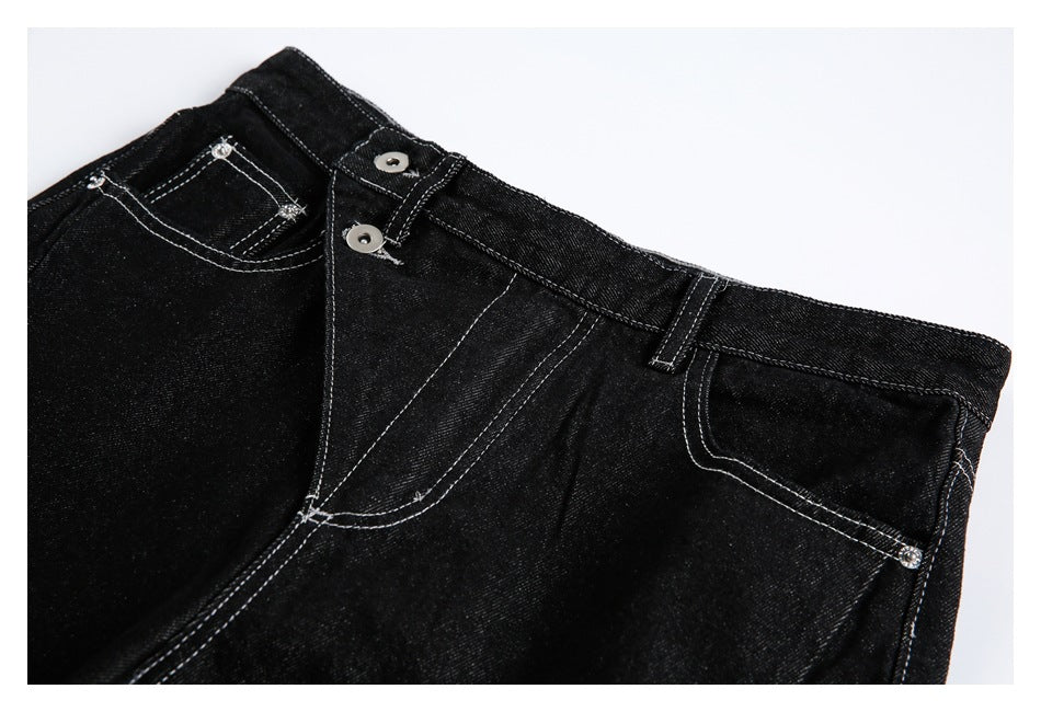 Close-up of black jeans showing the waistband, button fly, belt loop, and contrast-stitched front pockets.