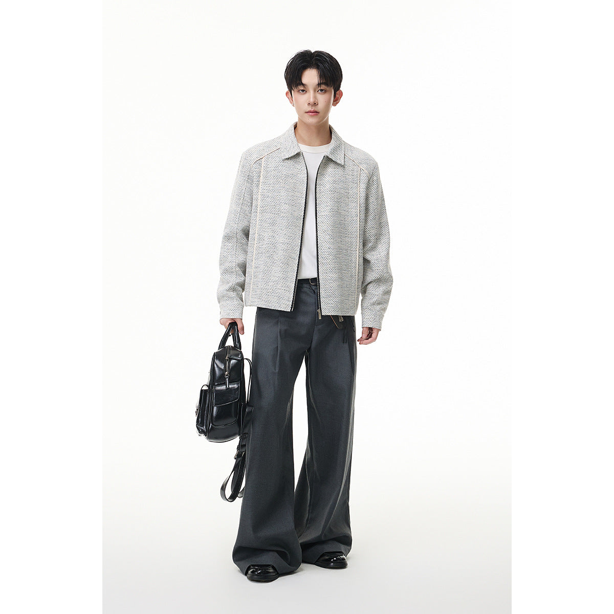 Full-length model wearing a light gray textured zip-front jacket with a white shirt and wide charcoal trousers, holding a
