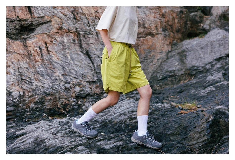 Side view of a person wearing yellow-green drawstring shorts while walking on rocky terrain.