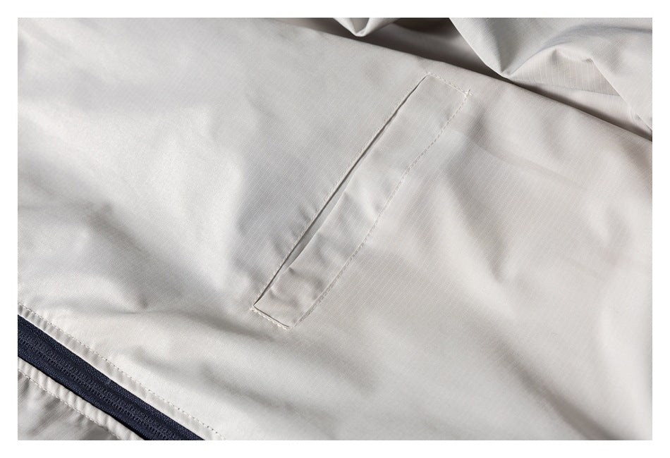 Close-up of an ivory jacket's welt pocket and dark navy zipper edge.