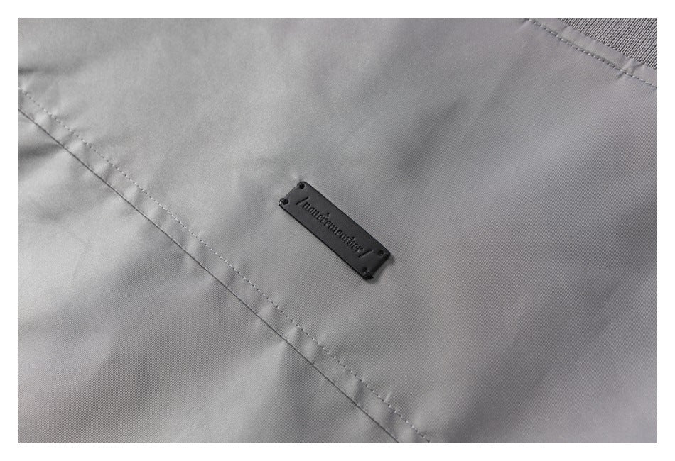 Close-up of a small dark logo patch sewn onto gray garment fabric.