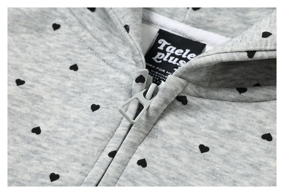 Close-up of a light gray heathered garment with scattered black hearts, a zipper pull, and a black neck label.