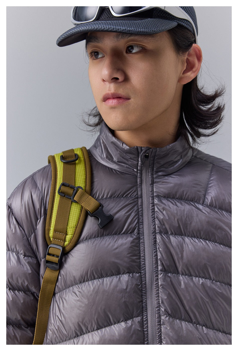 Close-up of a charcoal quilted jacket's stand collar and front zipper, with a lime backpack strap across the shoulder.