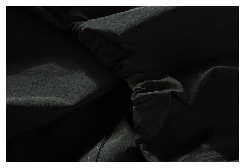 Dark close-up of black garment fabric showing gathered seams and folded construction.