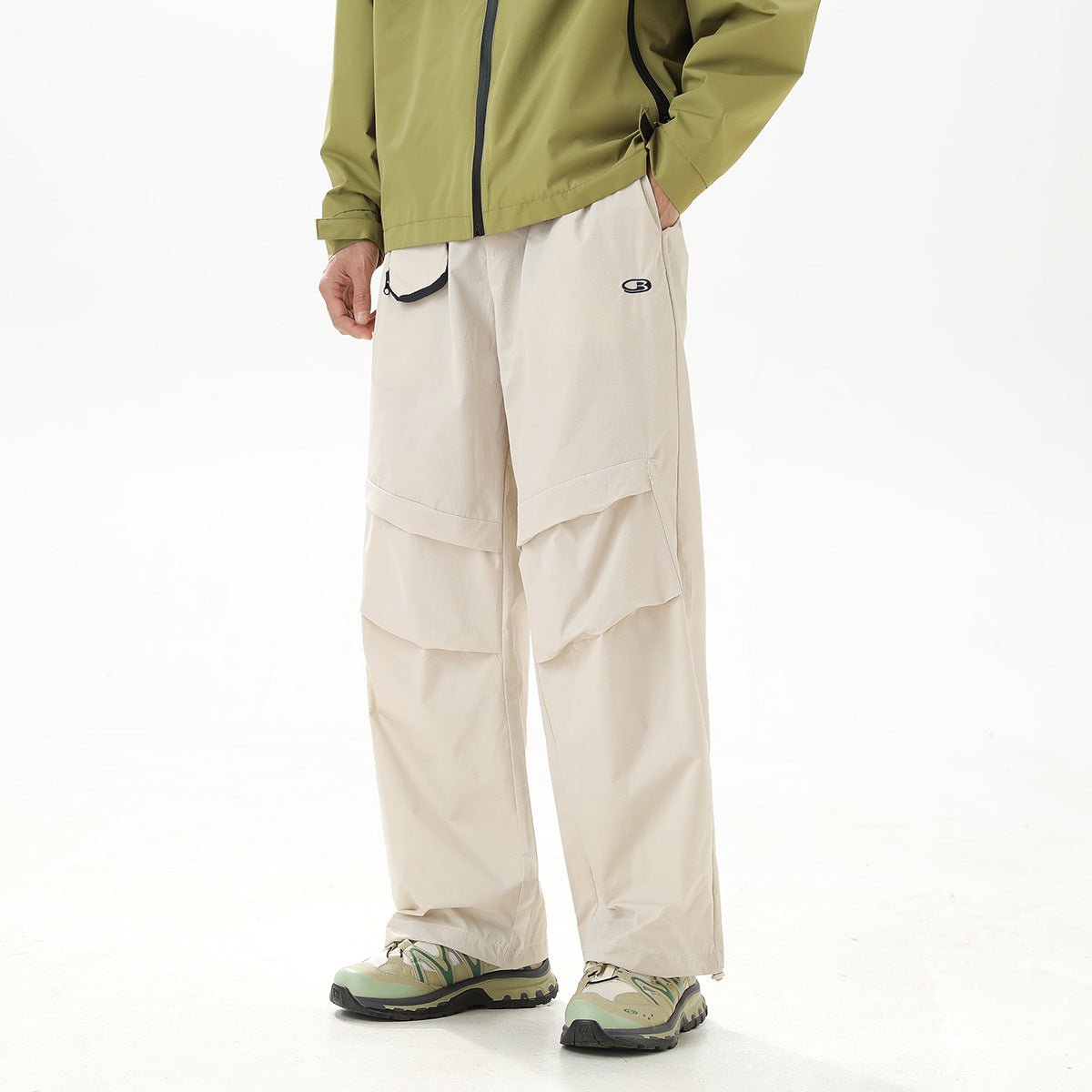 Cropped model wearing loose cream cargo pants with layered pockets and a small waist pocket.