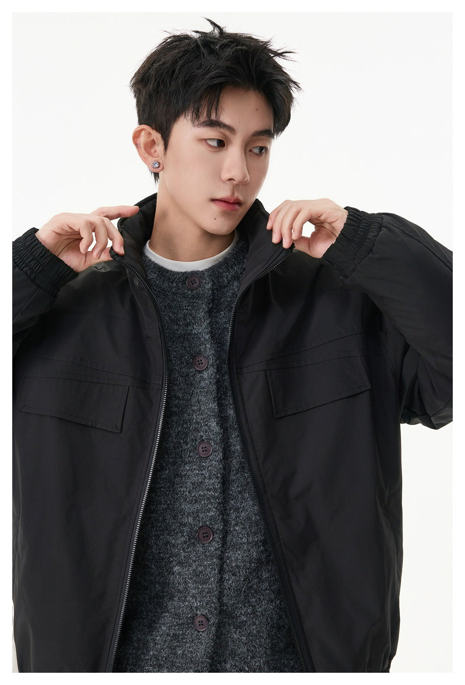 Close-up of a model wearing a black jacket, showing the raised collar, zipper, gathered cuff, and chest pockets.